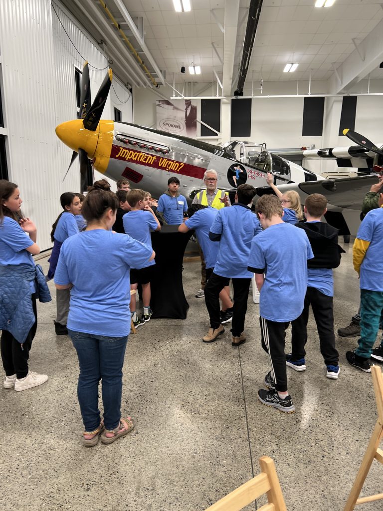 Group huddled listening to speaker in front of plane